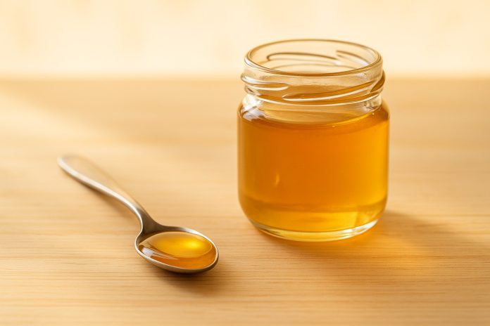 lingurita-miere.jpg Linguriță cu miere aurie pe masă lângă un borcan mic – obicei sănătos de seară pentru somn, imunitate și relaxare.