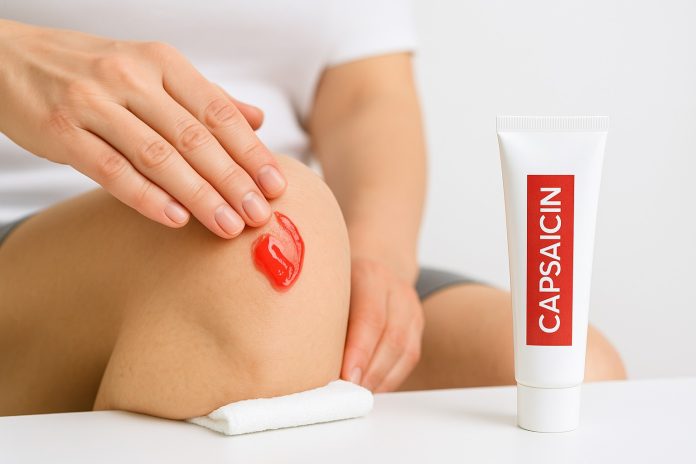 Persoană care aplică cremă cu capsaicină pe genunchi pentru calmarea durerilor articulare.