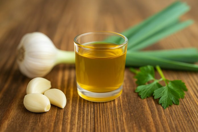 rachiu-usturoi-reteta.jpg Pahar cu rachiu de usturoi galben-auriu pe masă rustică, alături de căței și legătură de usturoi proaspăt cu frunze verzi