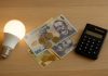 Cum să reduci factura la curent chiar de luna viitoare – 10 trucuri simple pe care le poți aplica imediat Bec LED aprins alături de bancnote și monede românești și un calculator de birou, simbol al economisirii la factura de curent