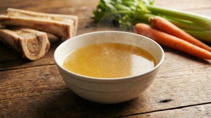 Bol cu supă de oase aurie, bogată în colagen, pe masă rustică cu legume.