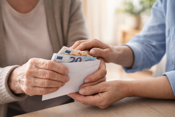 Mâinile unei persoane vârstnice ținând bani și documente, simbolizând creșterea indemnizației pentru însoțitor din 2026