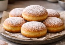 Gogoși pufoase prăjite, pudrate cu zahăr, așezate pe farfurie