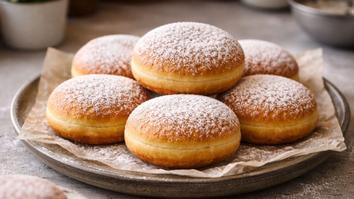 Gogoși pufoase prăjite, pudrate cu zahăr, așezate pe farfurie