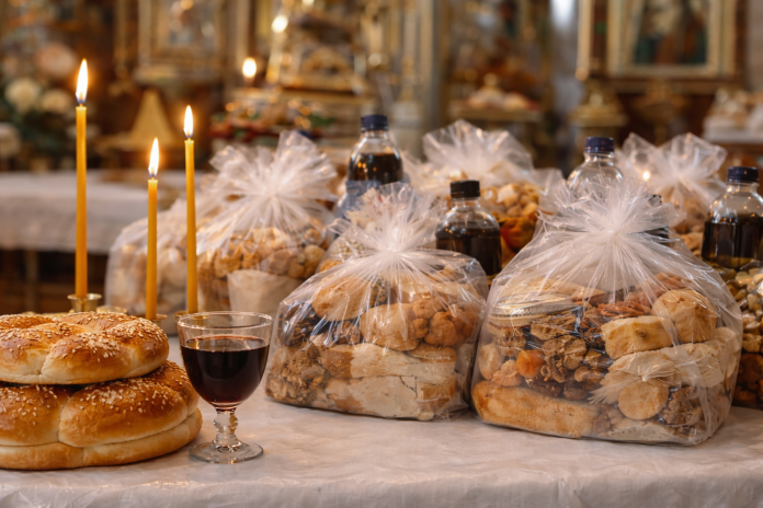 Lumânări aprinse alături de pachete de pomană tradiționale de Moșii de Iarnă pe masa din biserică