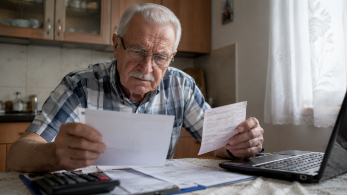 vesti-pentru-pensionari.jpg Pensionar analizând documente și informații financiare la masa din bucătărie