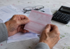 Guvernul acordă pensionarilor până la 1.000 de lei în două tranșe. Cine se încadrează Mâinile unui pensionar ținând un talon de pensie și documente financiare