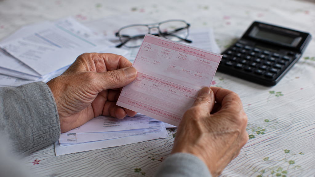 Mâinile unui pensionar ținând un talon de pensie și documente financiare