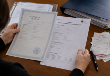 Mâinile unei persoane analizând documente pentru acordarea ajutorului de deces pe un birou.