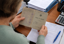 Persoană analizând carnet de muncă și documente de pensie pe un birou.