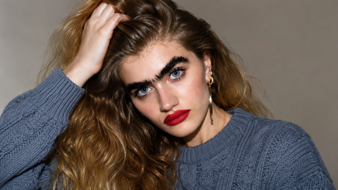 Model Sophia Hadjipanteli cu sprâncene naturale unite, portret fashion editorial, simbol al controverselor despre frumusețe.