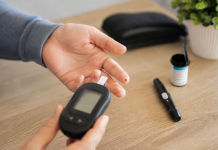 Persoană ținând un glucometru lângă mâna pregătită pentru măsurarea glicemiei, simbolizând depistarea diabetului de tip 2.