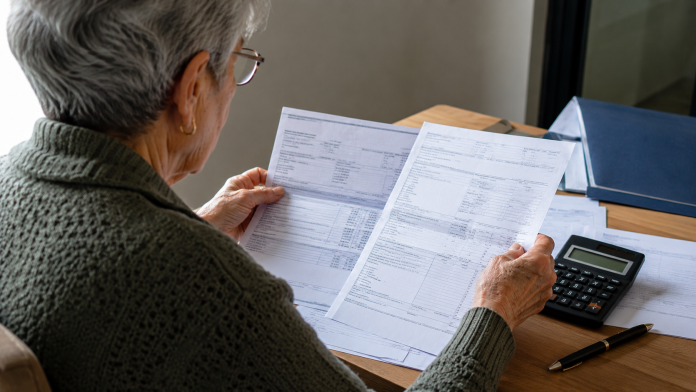 sprijin-pensionari-doua-transe-bani-2026.jpg Persoană vârstnică analizând documente de pensie, simbol pentru ajutor financiar în două tranșe pentru pensionari.