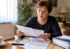 Vârsta de pensionare până în 2030: ce se schimbă pentru femei și bărbați. Tabelul corect pe care trebuie să-l verifici Femeie care verifică documentele privind vârsta de pensionare și calendarul pensiilor până în 2030.